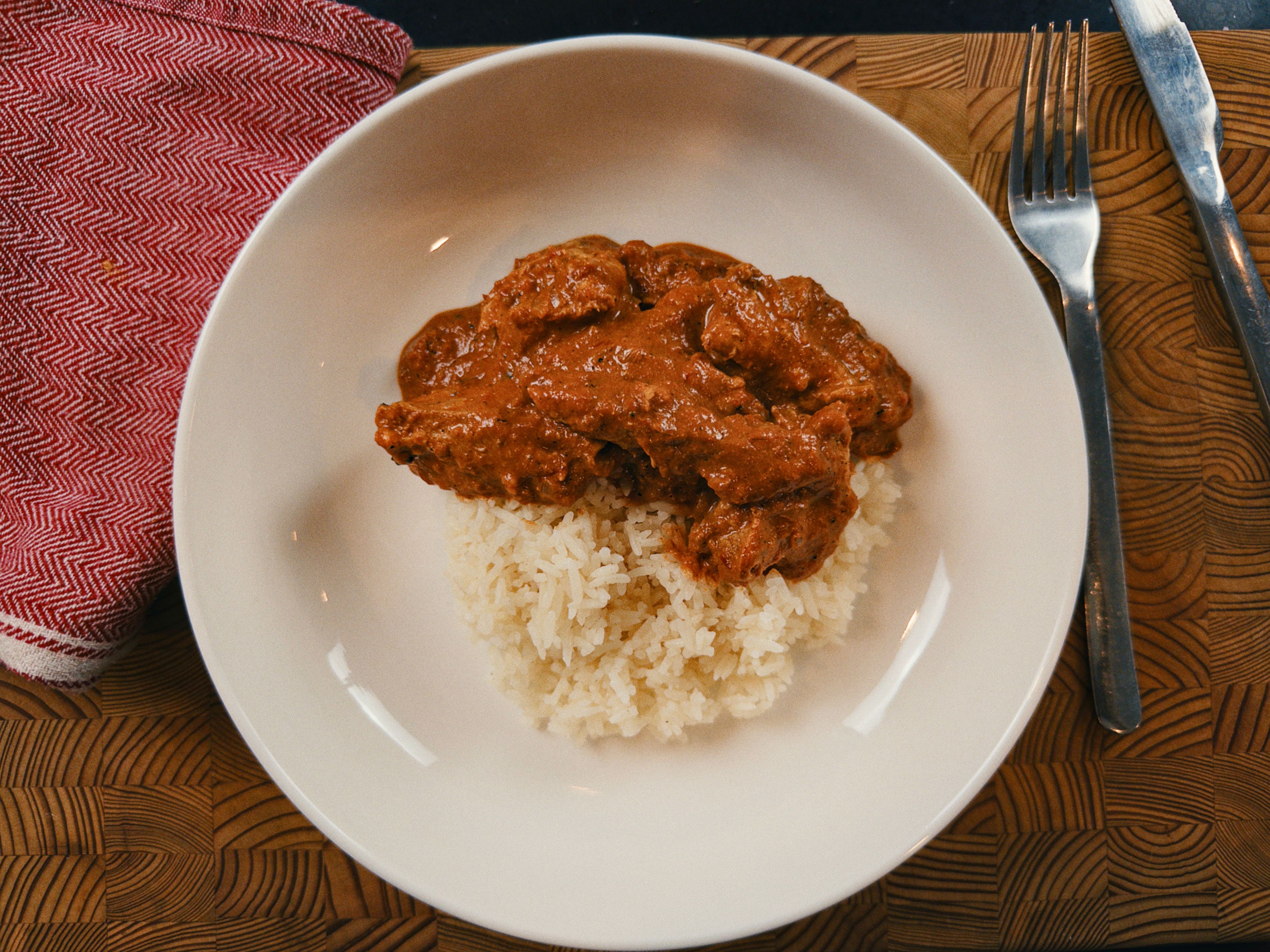 Frango ao molho cremoso de tomate e manteiga servido sobre arroz branco em um prato branco.