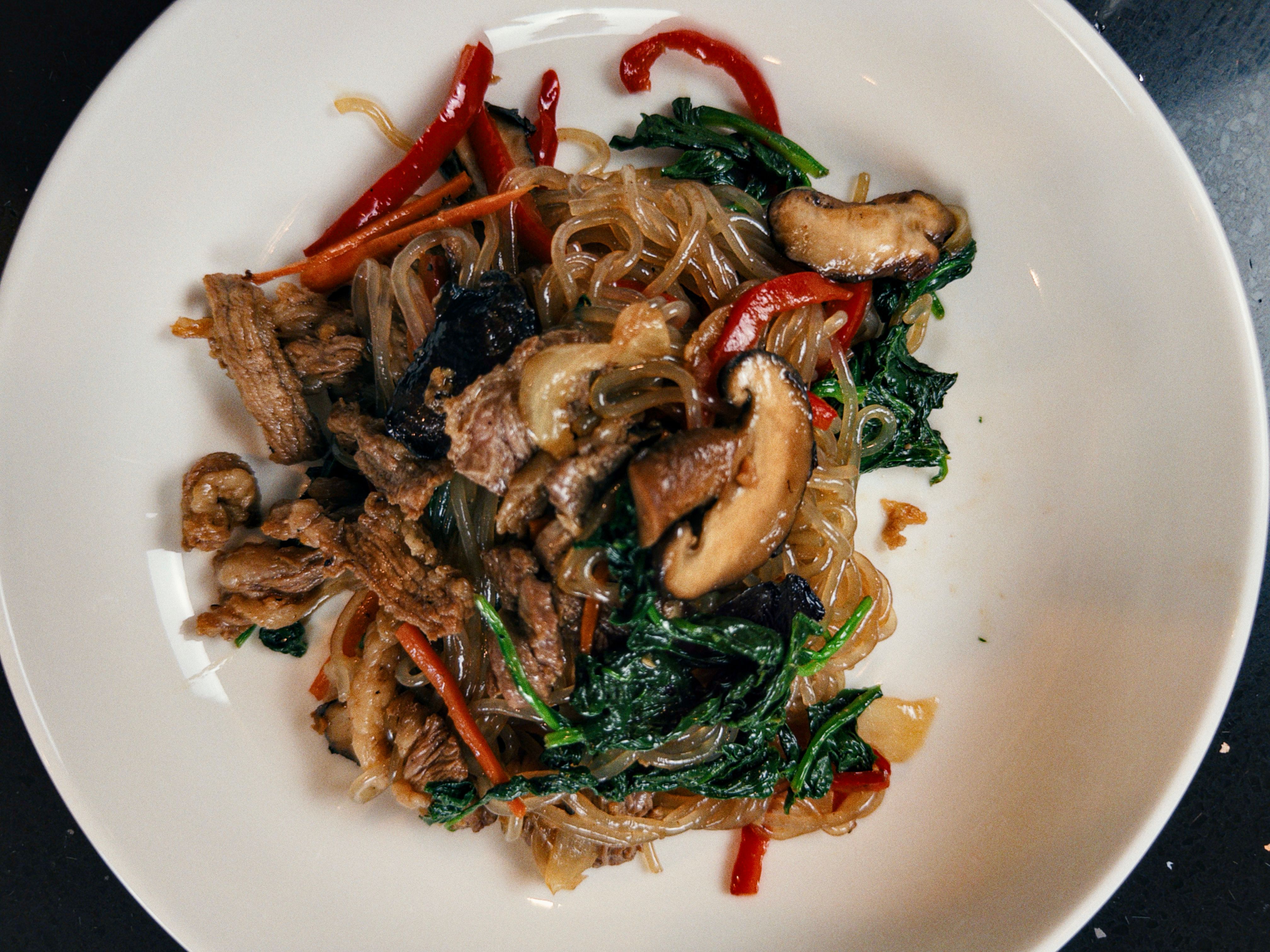 Japchae com carne bovina, macarrão de batata-doce, espinafre, pimentão vermelho e cogumelos em uma tigela branca