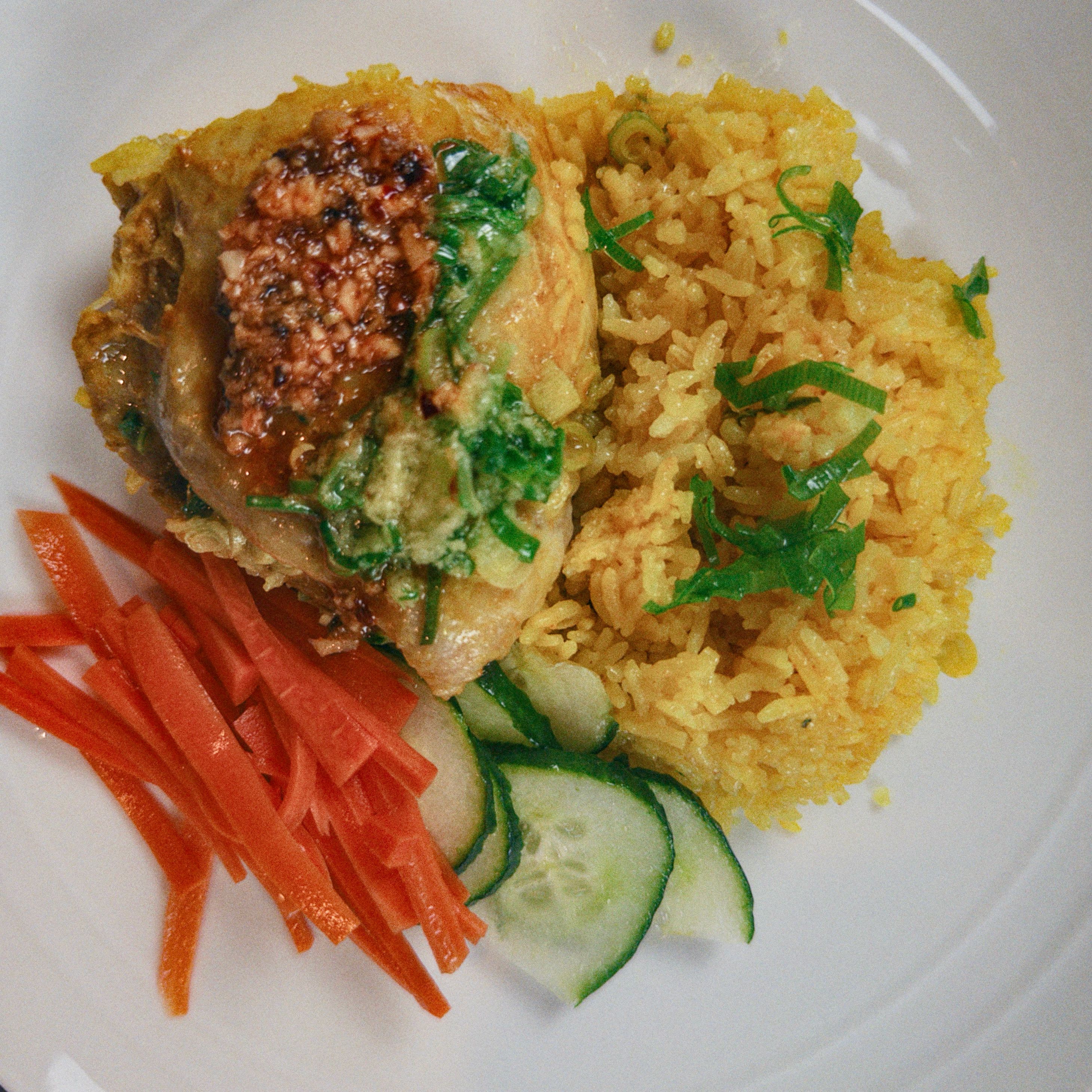 Frango à moda de Hainan servido com arroz dourado, pepino fatiado, cenoura e cebolinha