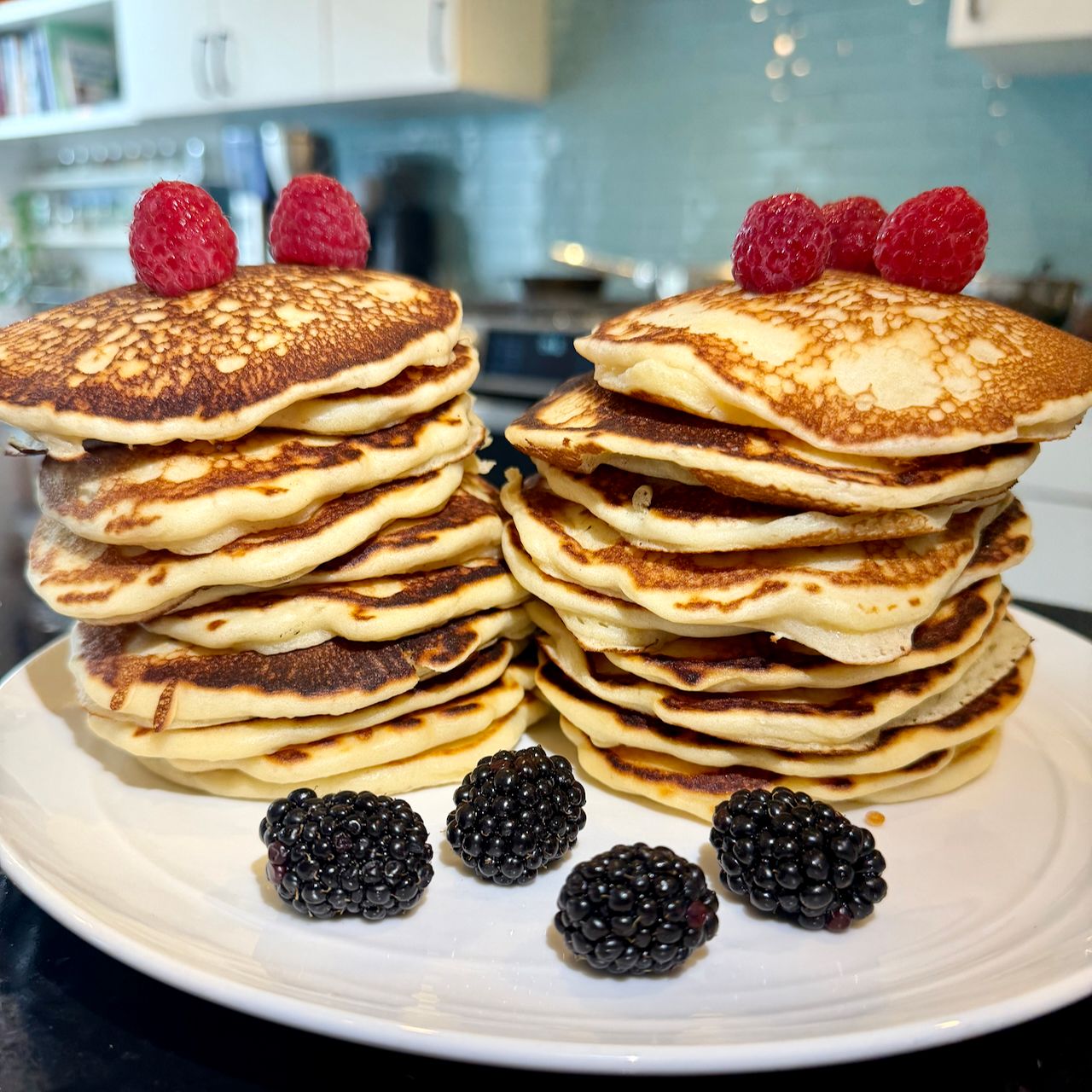Stacks of fluffy pancakes topped with raspberries and served with blackberries